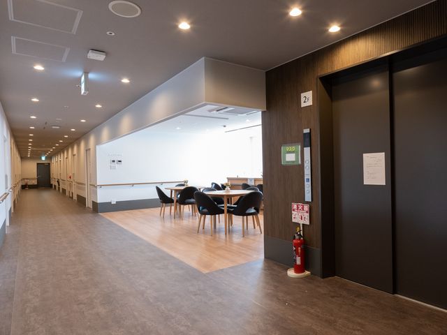 清潔感のある廊下と食堂 エレベーター こちらの職場では、明るく開放的な食堂で利用者さまとのコミュニケーションを楽しむことができます。余裕のあるスペースでのびのびと勤務頂けます。