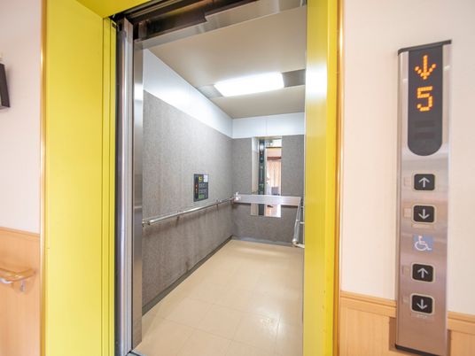 黄色い枠組みで縁取られたエレベーターである。内部は奥行きがあり明るく、壁面に手すりや鏡が設置されている。
