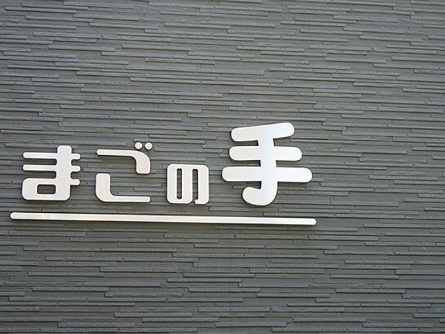 施設のシンボル看板 外壁 穏やかな色合いの壁面に、清潔感のあるデザインで施設名が掲げられています。訪れる方を温かく迎え入れる第一印象をお持ちいただけます。
