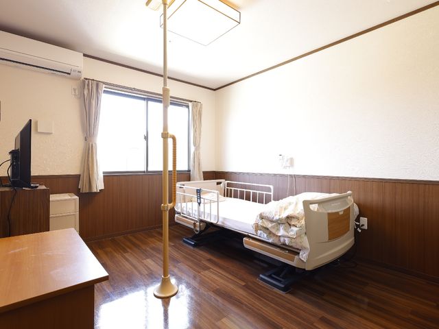 快適な居室の一角 居室 窓辺にあるベッドと生活の必需品が整えられた居室は、日当たりが良く落ち着いた雰囲気です。サポートが必要な方も安心してお過ごしいただける設計となっています。