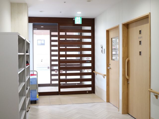 廊下とドアの明るい空間 玄関 手すりが設置された廊下は歩行に安全性を提供し、木目調のドアが温かみのある雰囲気を醸し出しています。