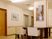 サムネイル 施設の写真 絵画がたくさん飾られた館内。左側には居室のドアが並ぶ廊下があり、右側には白い椅子がセットされたテーブルがあり、壁には手すりが付いている。