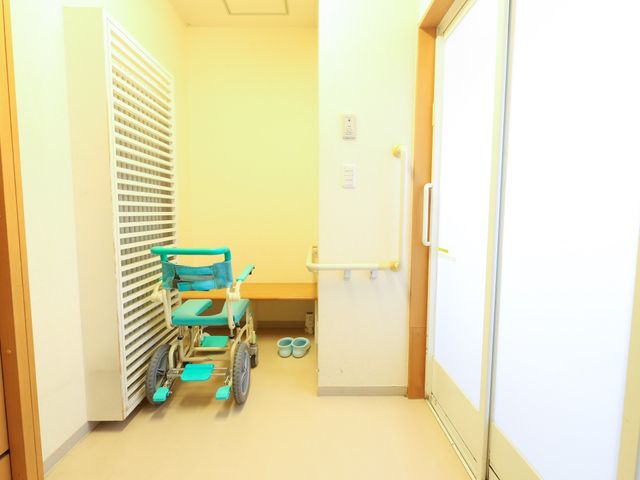 車椅子が置かれた廊下 脱衣所 清潔で明るい廊下に配置された車椅子は、出入りを容易にするよう配慮されている様子が見て取れます。手すりも設置され、安全に配慮された環境です。