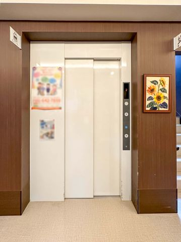 茶色い枠のエレベーター エレベーター 明るく清潔感のあるエレベーター前の空間です。壁に飾られたアートが、心地よい雰囲気を醸し出しています。