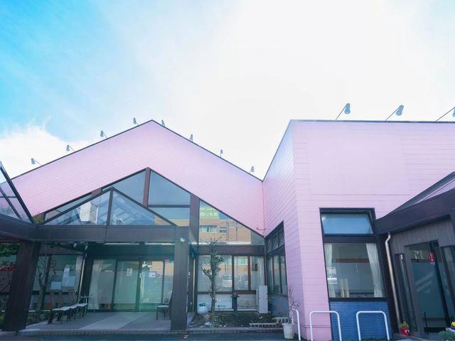 ピンク外壁の建物外観 外観   ピンク色の外壁が印象的な建物で、ガラス面が多く明るさを感じます。入口まわりも開放的で、働く場の雰囲気が伝わります。