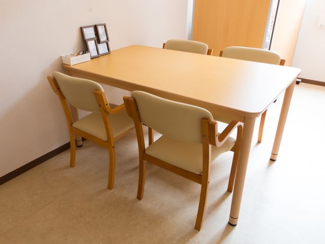 シンプルな木製のダイニングテーブル 相談室 ゆったりとした座り心地のダイニングチェアを備えた食卓スペースです。心地よい光を受けながら、食事やコミュニケーションを楽しめる環境が提供されています。