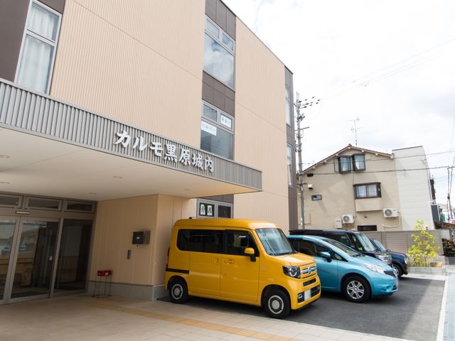 施設前のエントランス風景 外観 広々とした前庭には送迎用の車が停まり、出入りしやすい自動ドアが設置されています。