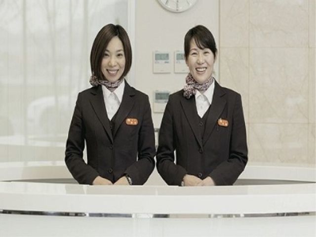 笑顔のスタッフとカウンター スタッフ 温かい笑顔でお迎えする清潔感のある受付フロントです。お客様の対応を丁寧に行う姿勢が伝わります。