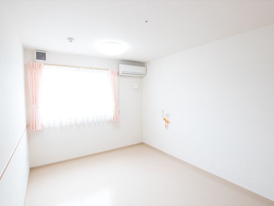白を基調とした明るく爽やかな雰囲気の居室は、シンプルな内装になっている。オレンジ色のコードが、右側の壁に付いている。