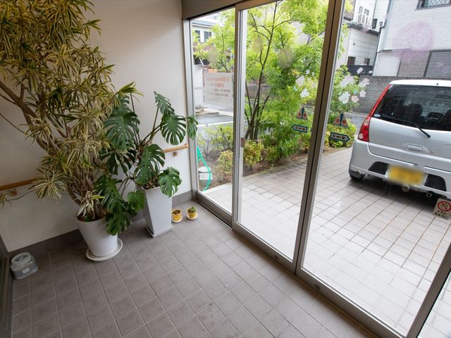 緑ある出入口の一景 エントランス 緑あふれるエントランスからの眺めは、訪れる方々に安らぎを提供します。足元に生活感を感じる一足が優しく出迎えてくれます。