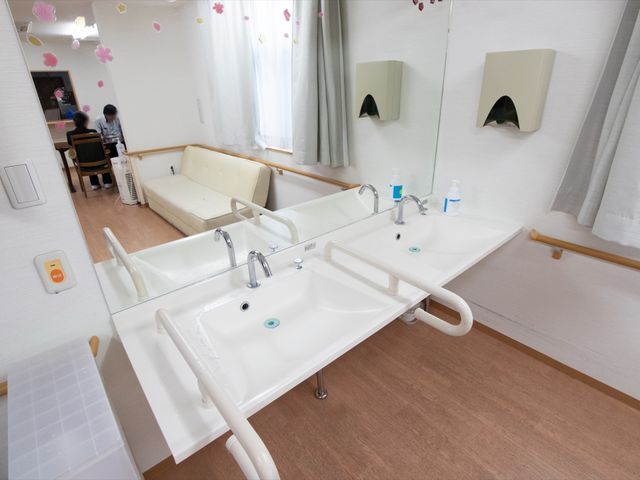 手すり付き洗面台 洗面台 柵のついた洗面台があり、背後にはソファやテーブルが備わった落ち着いた雰囲気のスペースが確保されています。安心して日々の暮らしを送れる環境が整っています。