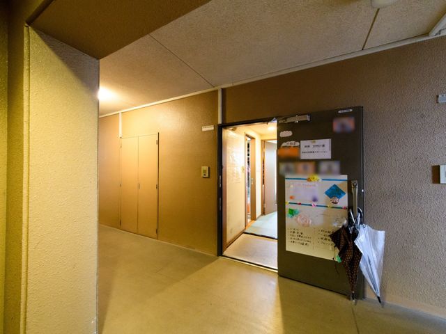 廊下と掲示物のある入口 玄関 入口には色とりどりの掲示物が飾られ、温もりのある迎え入れがされています。壁には傘が掛けられ、訪れる人々の小さな配慮が垣間見えます。