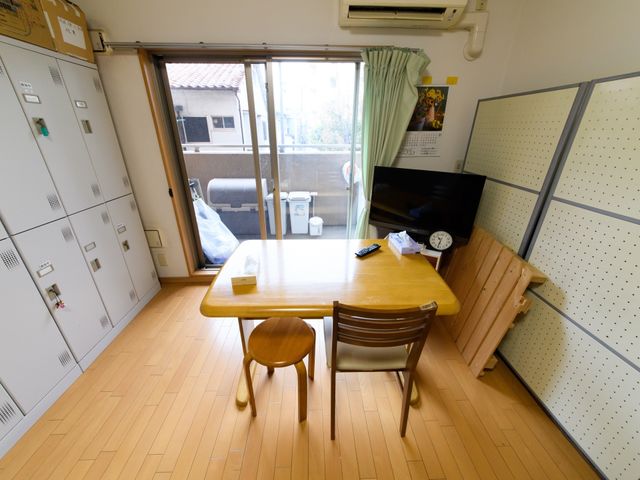 共有スペースの居室 スタッフルーム 落ち着いた雰囲気の居室で、大きなテーブルが中心にあります。日差しの入る窓側には快適に過ごせるスペースが確保されています。