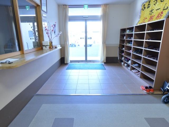 エントランスと靴棚 玄関 広々として明るい入口は、利用者様の出迎えに最適な空間です。靴を収納する棚が整然と配置され、清潔感が感じられます。