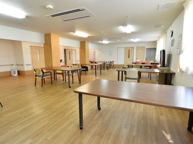 広々とした共有スペース 共有のリビング 木目調の床材を使用した明るく広い空間で、ゆったりとコミュニケーションを取りながら食事ができるダイニングエリアです。複数のテーブルと椅子が配置され、居心地の良い雰囲気を醸し出しています。