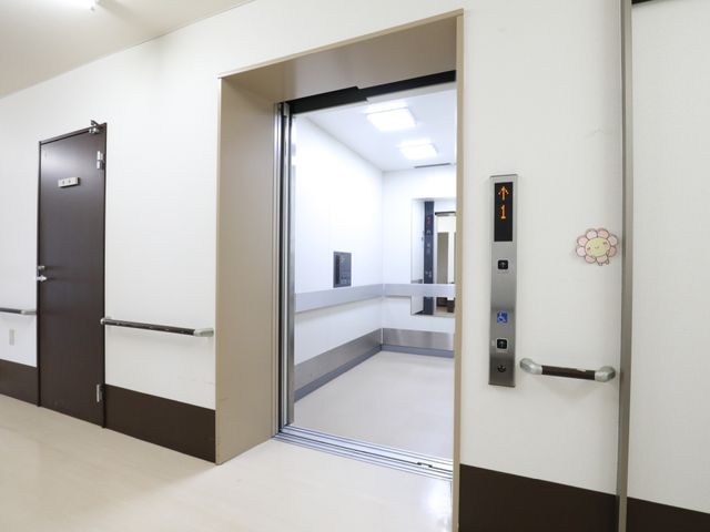 清潔なエレベーターホール エレベーター 広々としたスペースには手すりが備わり、バリアフリー設計でご利用者様の移動が楽になっています。白と茶色の色使いが落ち着た雰囲気を醸し出しており、快適な環境でのお仕事が期待できます。