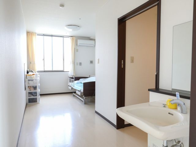 洋室と洗面所 居室 明るく清潔な個室で、シンクがついた洗面台も完備され、プライバシーに配慮されています。自分の時間を大切にしながらも、サポートが近くにある安心感を得られます。