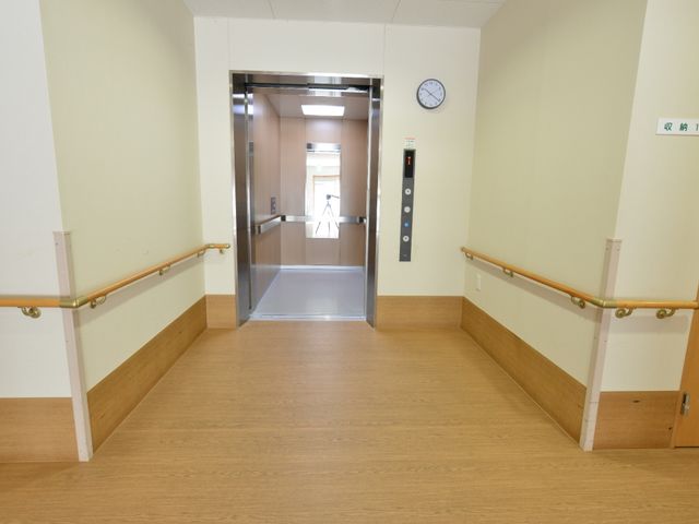 手すり付廊下とエレベーター エレベーター前 手すりが設置された廊下に面したエレベーターがあり、安全に移動できる配慮がされています。明るく清潔感のある通路は、働く環境としても快適です。