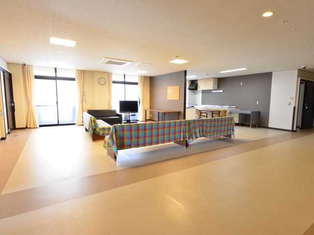共用スペースの角部屋 館内 ゆとりあるリビングでは、居心地の良いソファやテーブルが配置され、明るい日差しの中で寛げます。キッチンも隣接し、交流の場として最適です。