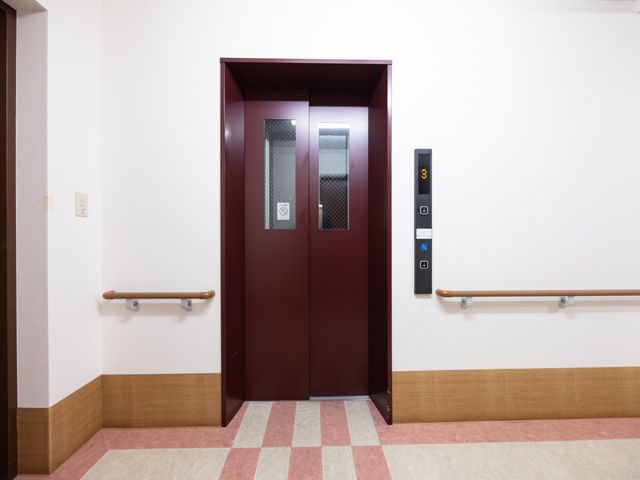 手すり付きのエレベーター扉 エレベーター 手すりが設置されたエレベーター前の廊下が見られます。ご入居者様の移動をサポートします。