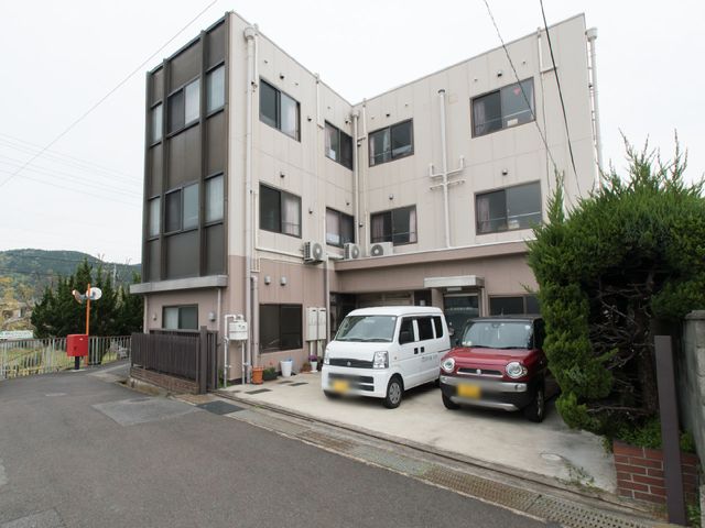 施設前の庭と駐車場 施設の立地 明るい色合いの建物前には広々とした駐車スペースが整備されており、来訪者の利便性を考慮した設計となっています。