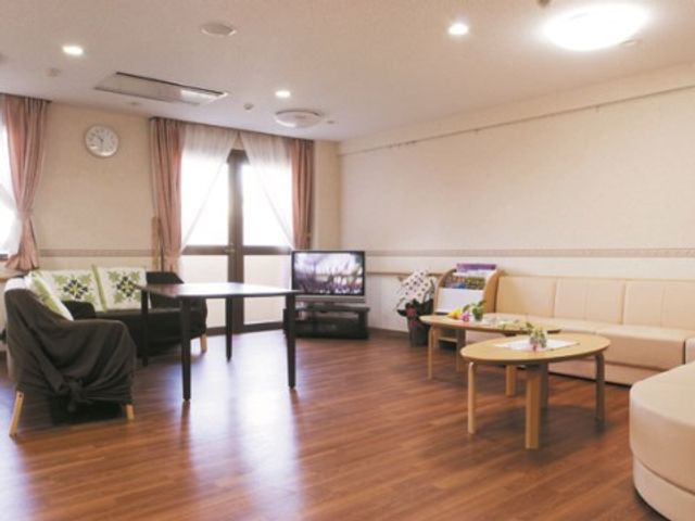 明るい共有リビング空間 談話スペース 広々としたリビングには、ゆったりくつろげるソファやテレビが設置され、明るく開放的な雰囲気です。植物のあるテーブルが彩りを添え、訪れた方々の憩いの場となっています。