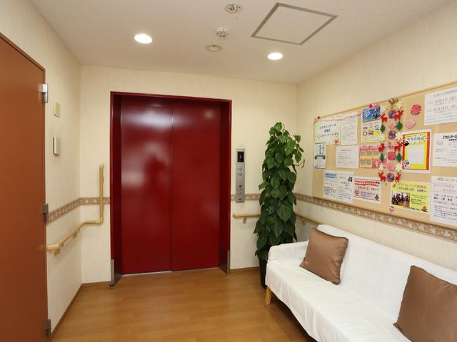 赤いエレベーターと掲示物 エレベーター 赤い扉のエレベーターと情報が満載の掲示板が設置された待合スペースです。心地良い安らぎの空間がここに広がっています。