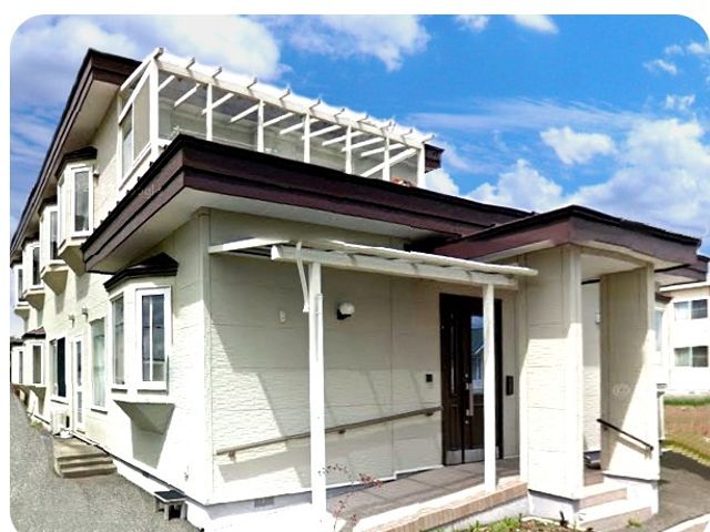 施設の外観 外観   青空の下に建つ、白い外壁と屋根付きの出入口が目を引く建物です。周囲の通路も見え、落ち着いた雰囲気です。