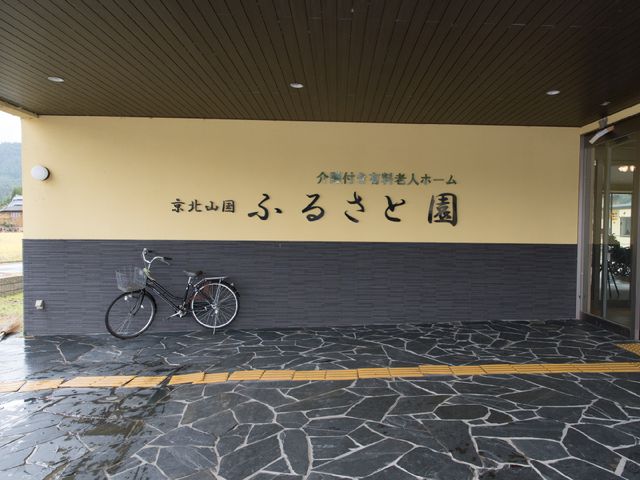 エントランス看板付き壁面 施設ロゴ 温かみのある色合いの入口に設置された看板は、訪れる方々を優しく迎え入れます。自転車が停められるこのスペースは、来訪者の利便性を考慮して設計されています。