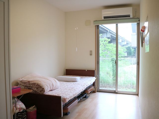 居室のベッドと窓 居室 ひだまりのような暖かさを感じる居室です。窓からは自然光が入り、明るい雰囲気が演出されております。