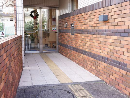 玄関前は煉瓦の塀に囲まれていて、足元には点字ブロックがある。ドアにはクリスマス用のリーフが飾られている。