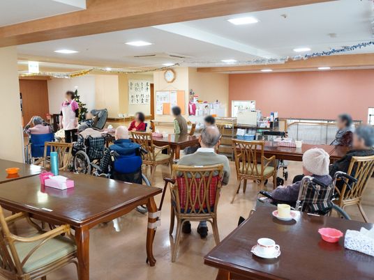 広々とした食堂に沢山のテーブルと椅子が置かれている。テーブルの上にはティッシュボックスがある。壁には入居者様の書道が貼られている。