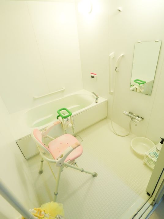 白色を基調とした浴室にシャワーチェアが置いてある。浴槽の手前側と奧の壁面に手すりが取り付けられている。