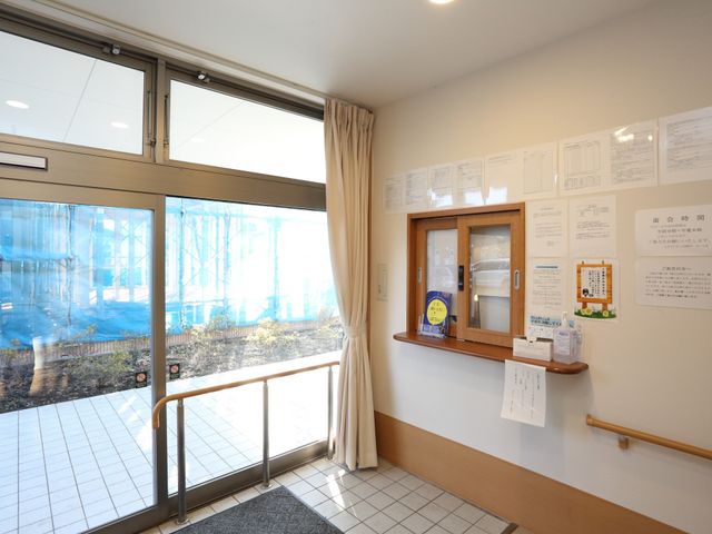 窓から自然光差し込む廊下 受付 明るい陽光が差し込むエントランスです。掲示物が整然と配置され、情報共有の場としても機能しています。