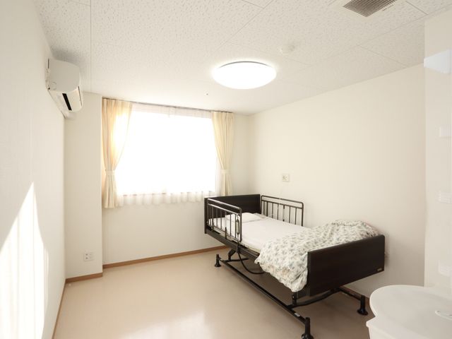 明るい個室のベッドと窓 居室 ゆったりとした個室は、日差しが入る窓側にベッドを配置し、快適な休息を提供します。