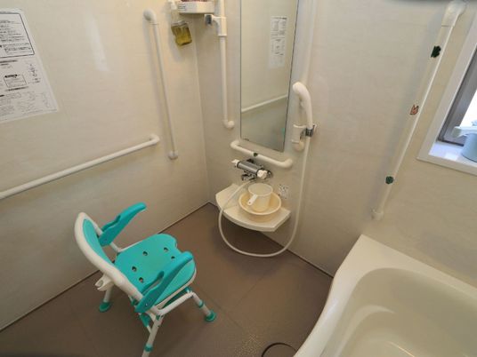 ユニットバスや窓が設置された浴室である。壁には手すりが取りつけられ、洗い場にはバスチェアーが置かれている。