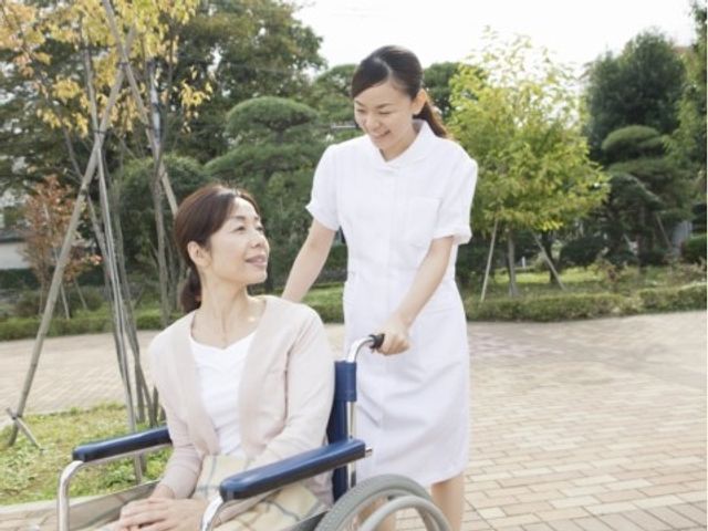 車椅子の利用者とスタッフ 笑顔で車椅子を押すスタッフとリラックスした表情をされている方が、緑豊かな中庭にいます。快適な外の空気を感じながら、ゆったりとした時間の流れを提供しています。