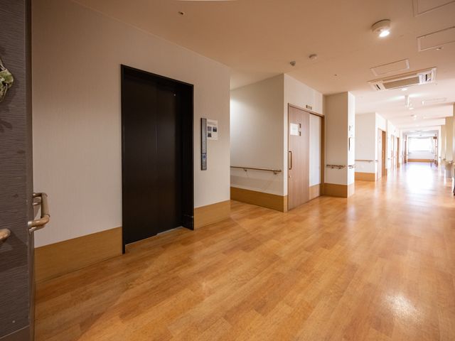 広々とした廊下 廊下 ゆったりとした通路は、木目調の床と壁が温もりを感じさせ、安心してお過ごしいただける環境を提供しています。
