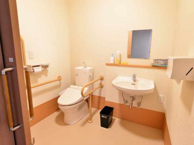 バリアフリーのトイレ設備 トイレ 手すり付きで安全に配慮された清潔なトイレです。明るく使いやすい環境で、利用者の快適さを支援します。