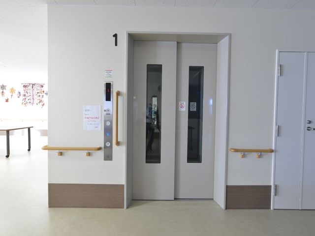 明るい共有スペースのエレベーター エレベーター 手を添えやすい高さの手すりが備わったエレベーターです。壁に掲示された美しい手作りアートが、訪れる人の目を楽しませてくれます。