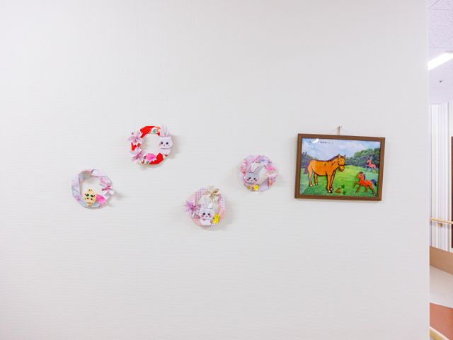 壁面飾りの廊下 廊下   白い壁に手作りの飾りと額絵が並び、明るくやわらかな印象です。歩くたびに季節感を感じられる通路です。