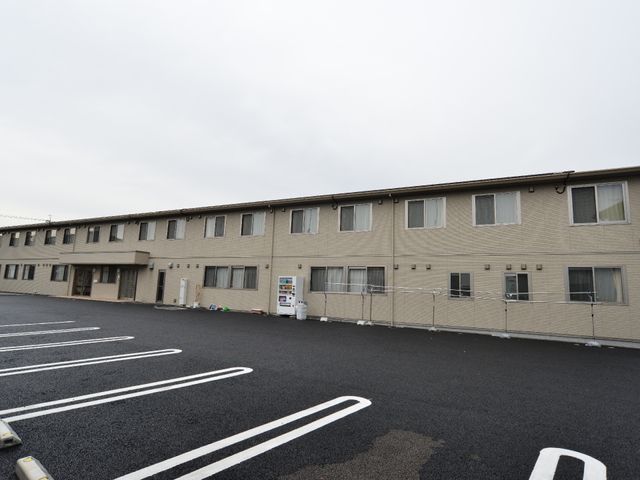 広々とした駐車場の建物 施設外観 ゆとりのある駐車スペースを確保した落ち着いた色合いの建物です。働きやすい環境を整え、日々の業務に集中できるようになっています。