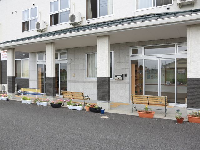 エントランス前のベンチと植物 外観 庭に彩られたベンチが並ぶ開放的なエントランスです。ゆったりとした雰囲気で訪れる方々を迎え入れています。