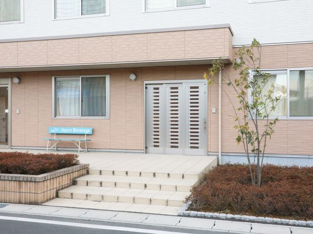 ピンクの壁の建物入口 スライドショー 清潔感のあるエントランスが迎えてくれる明るい建物です。いつでも訪れる人を温かく迎えるために準備されたベンチがあります。