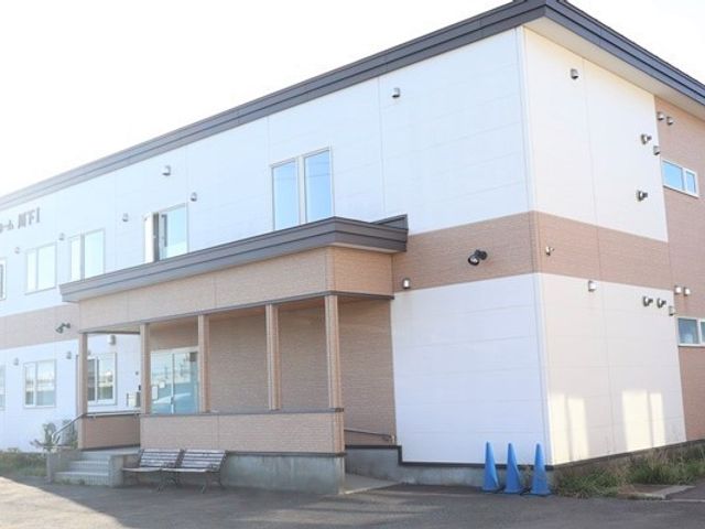 白壁の建物とエントランス 外観 広々としたエントランスは清潔感があり、ベンチも設置されて心地よい待合スペースです。