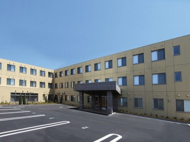 広々とした建物の外観 施設外観 駐車スペースが整備された清潔な建物です。朝日に包まれて温かい印象を与え、訪れる方々を優しく迎え入れます。