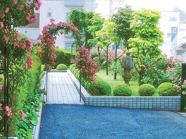 花咲く庭園の通路 庭   花や緑に囲まれた庭で、木の通路が奥へ続いています。気分転換や散歩を楽しめる、落ち着いた雰囲気です。
