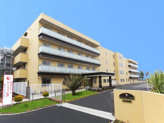 建物外観 外観   青空の下に、バルコニーが並ぶ落ち着いた外観です。駐車しやすい広い前面スペースも見えます。