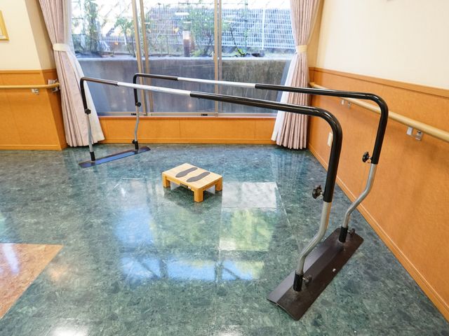 訓練用の器具と床 共有スペース 手すりと段差が設けられ、機能回復をサポートする空間です。明るい窓辺で気持ちよく訓練が可能です。