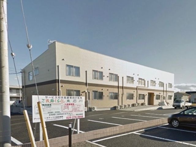 明るい空の下の外観 デイサービス 広々とした駐車場が整備された建物です。陽光に照らされて、明るく開放的な雰囲気を感じられます。